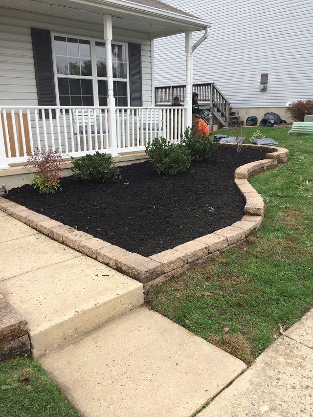 Front yard with a brick-edged flower bed filled with black mulch, shrubs, and a porch.