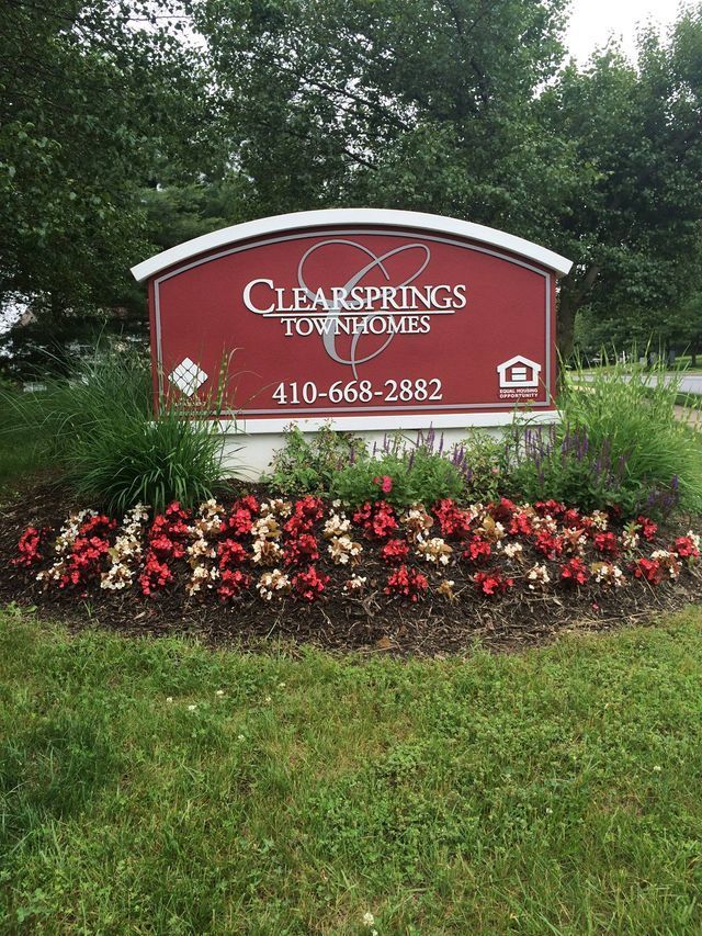 Sign for Clearsprings Townhomes, red with white trim, flowers in front, phone number visible.