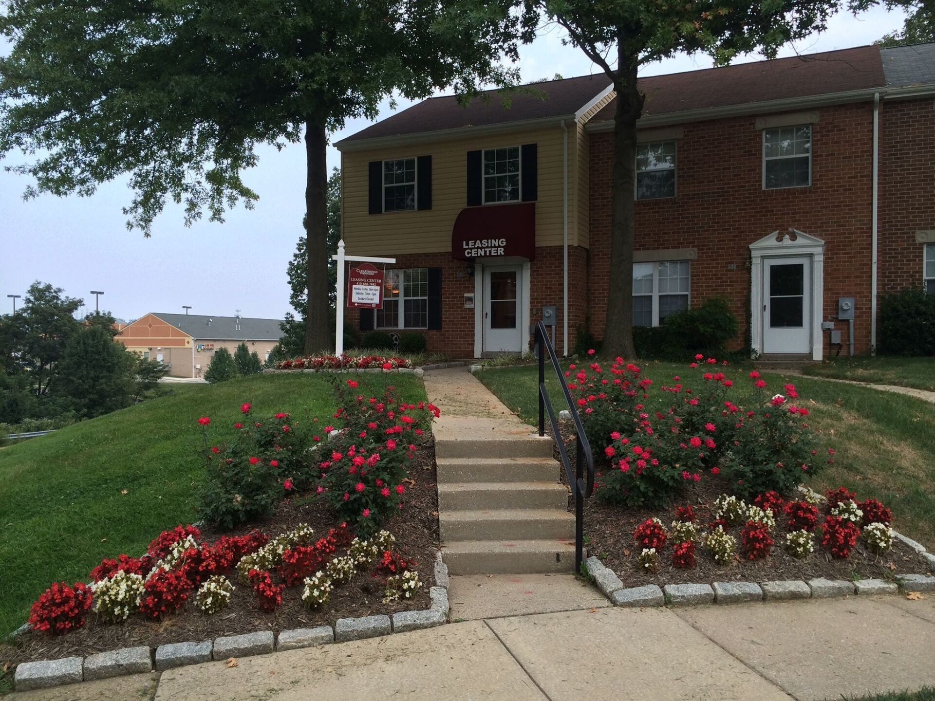 Townhouses with landscaped path, steps, and sign. Red and white flowers line the walkway.