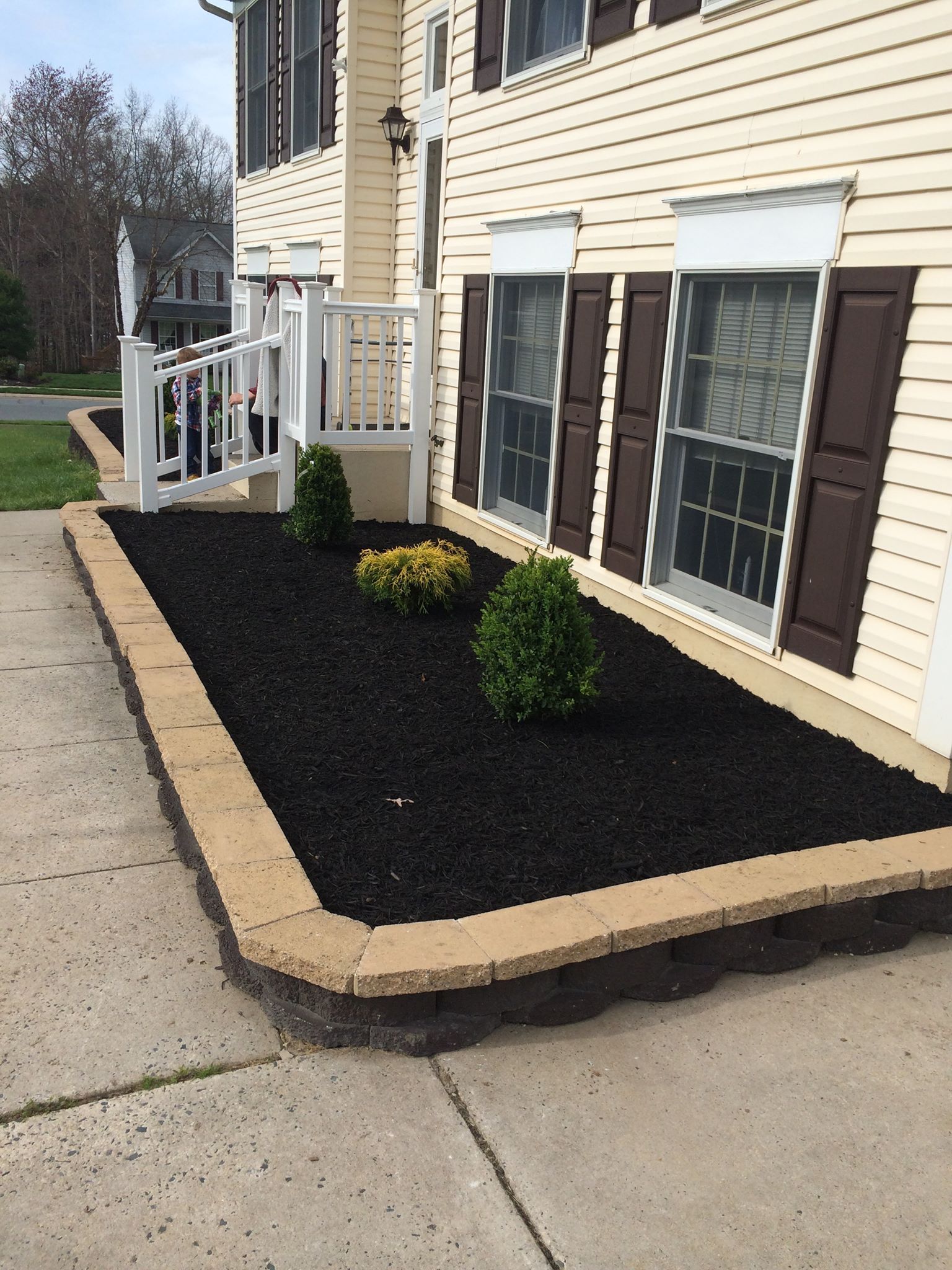 Beige house with black mulch flower bed and tan retaining wall.