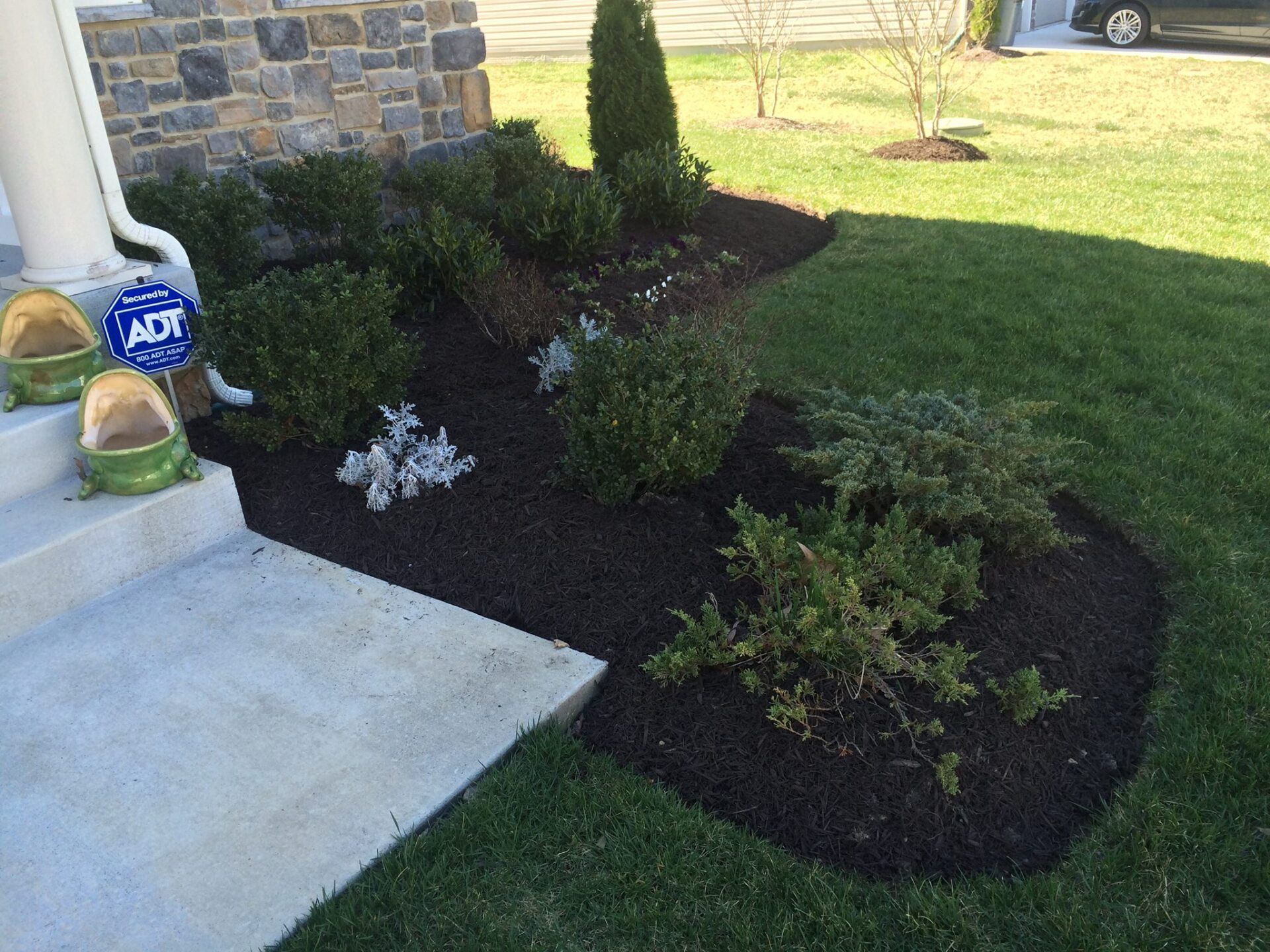 Landscaped front yard with dark mulch beds, green shrubs, and a lawn.