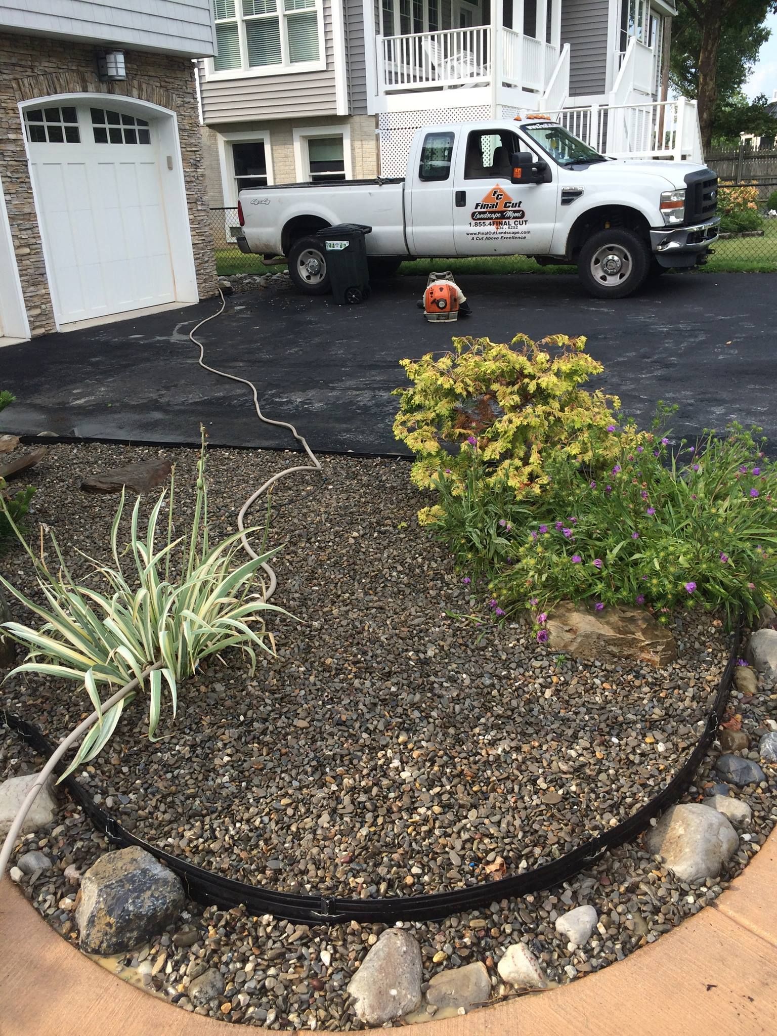 A white pickup truck parked on a driveway near a garden bed with landscaping.