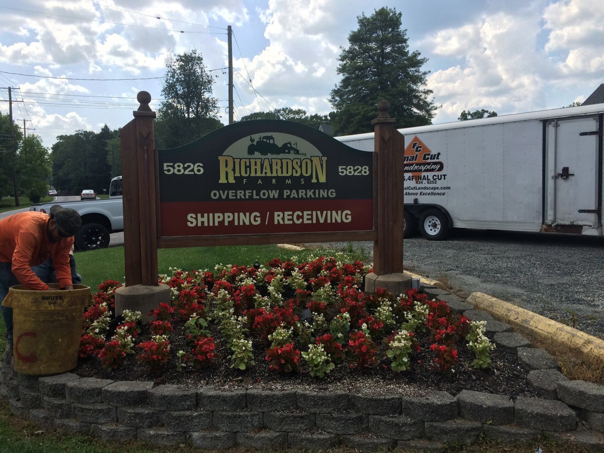 Sign for Richardson's with overflowing parking, shipping/receiving, and person gardening in front of flowers.