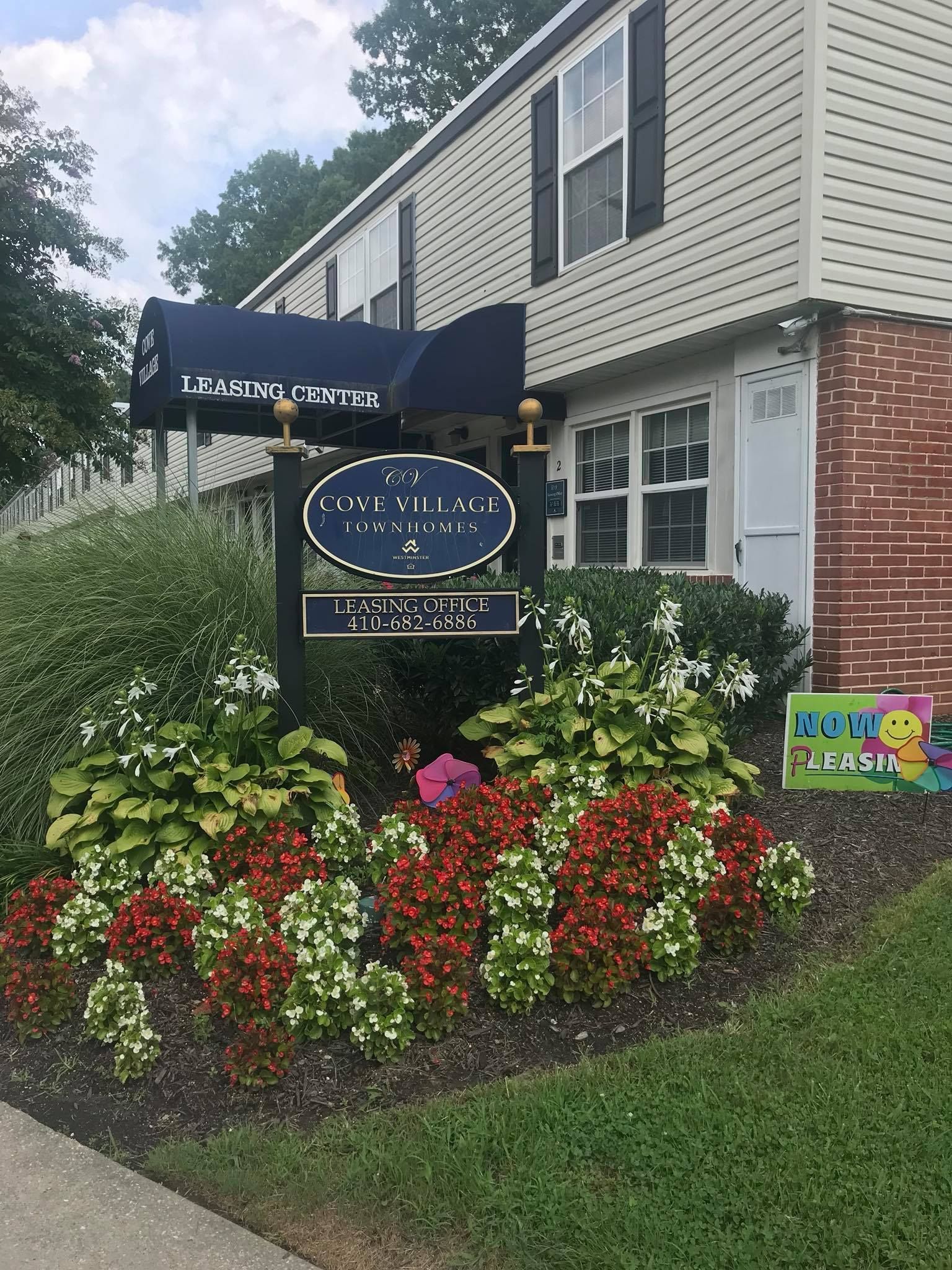 Sign for an apartment complex with flowers. Building in background, blue awning.
