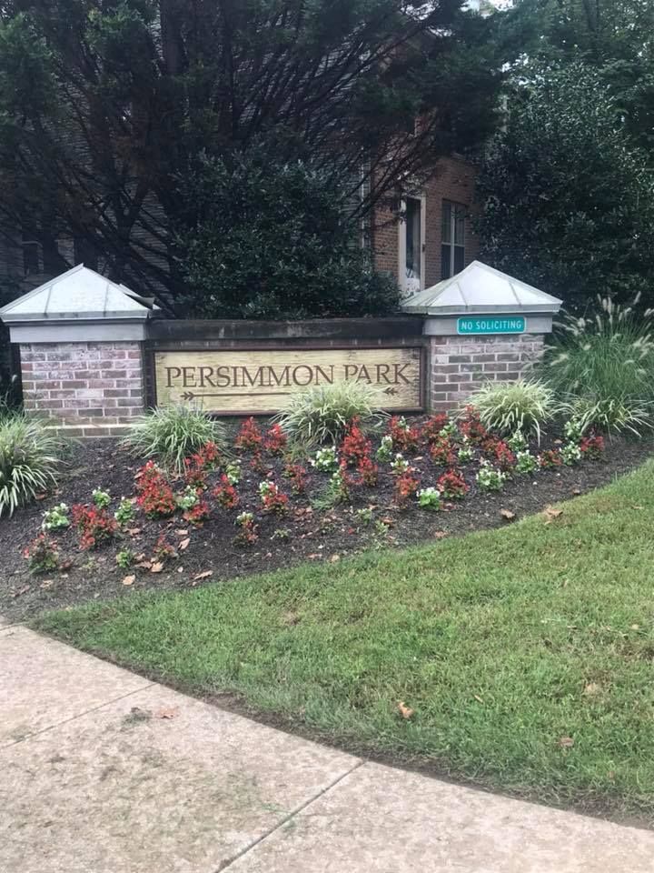 Sign for Persimmon Park with brick pillars, tan lettering, and flower bed.