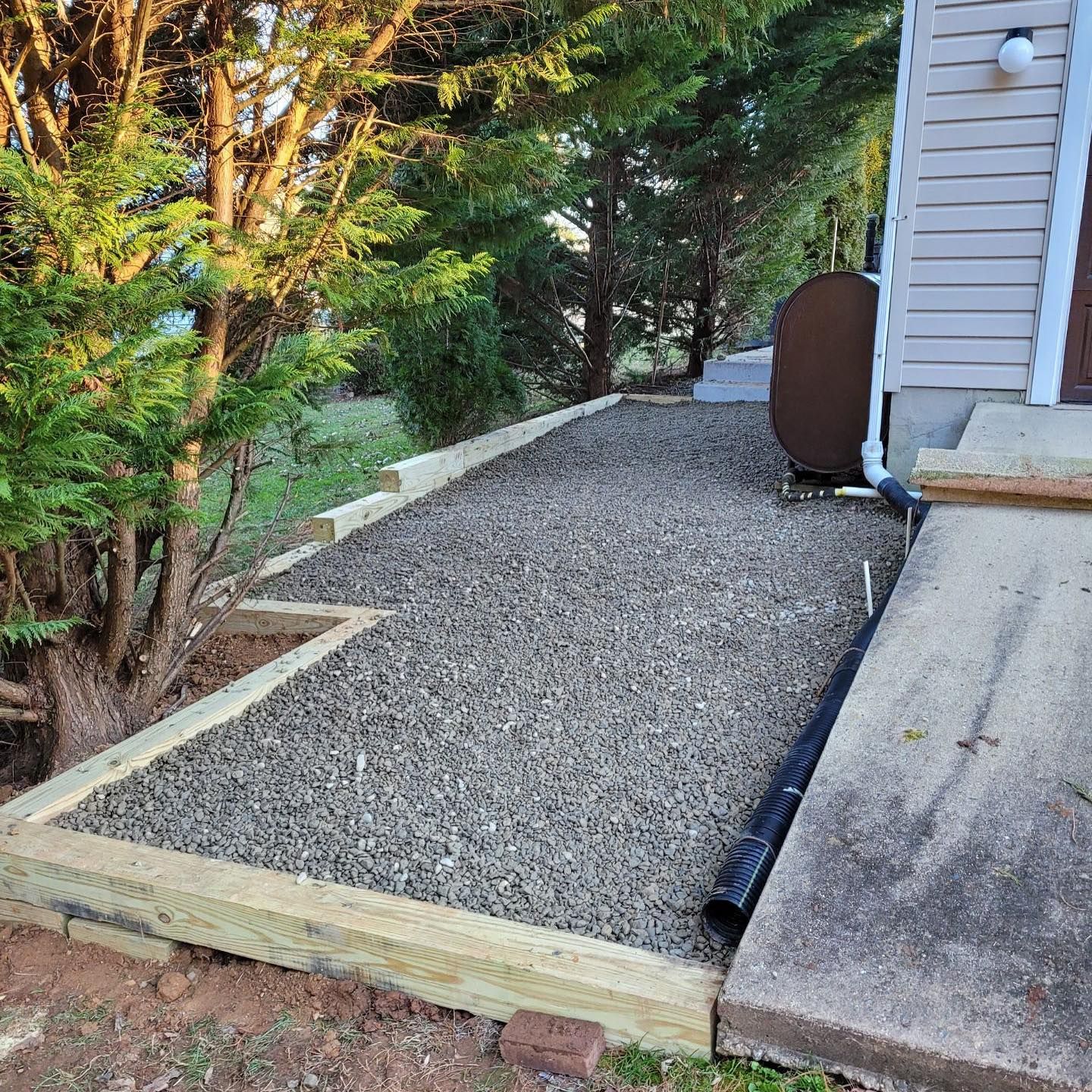 Gravel walkway next to a building, bordered by wooden beams. A tree is to the left.