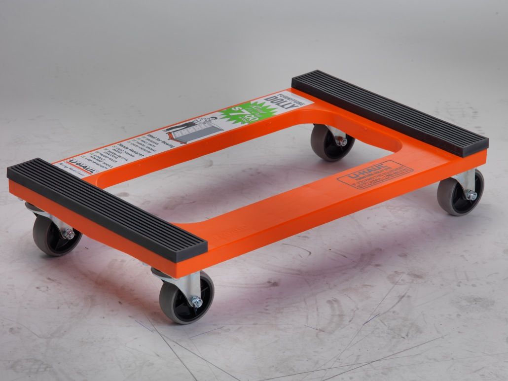 an orange moving dolly with black wheels is sitting on a concrete surface .