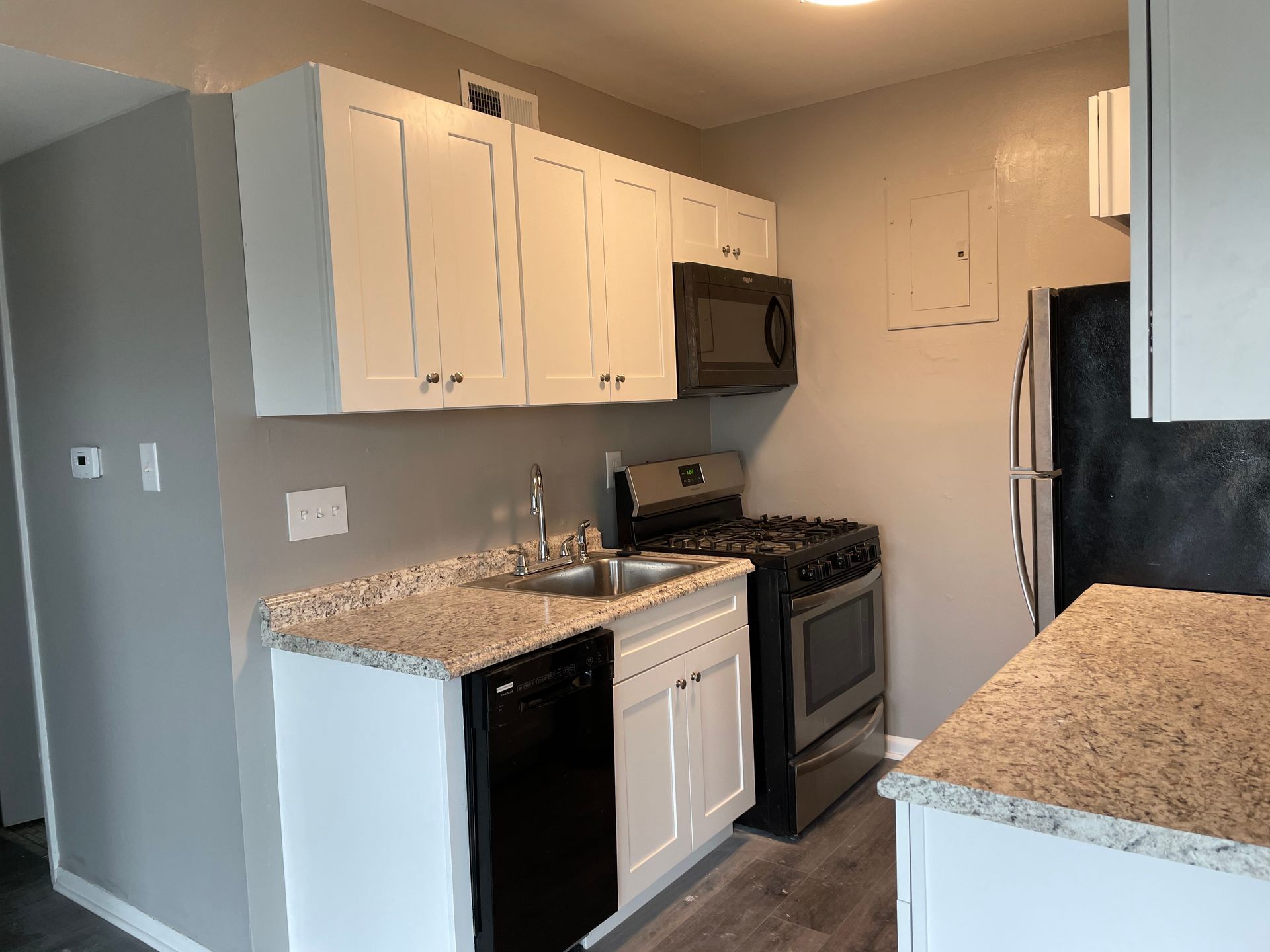 A kitchen with white cabinets , a stove , a refrigerator , a sink , and a microwave.