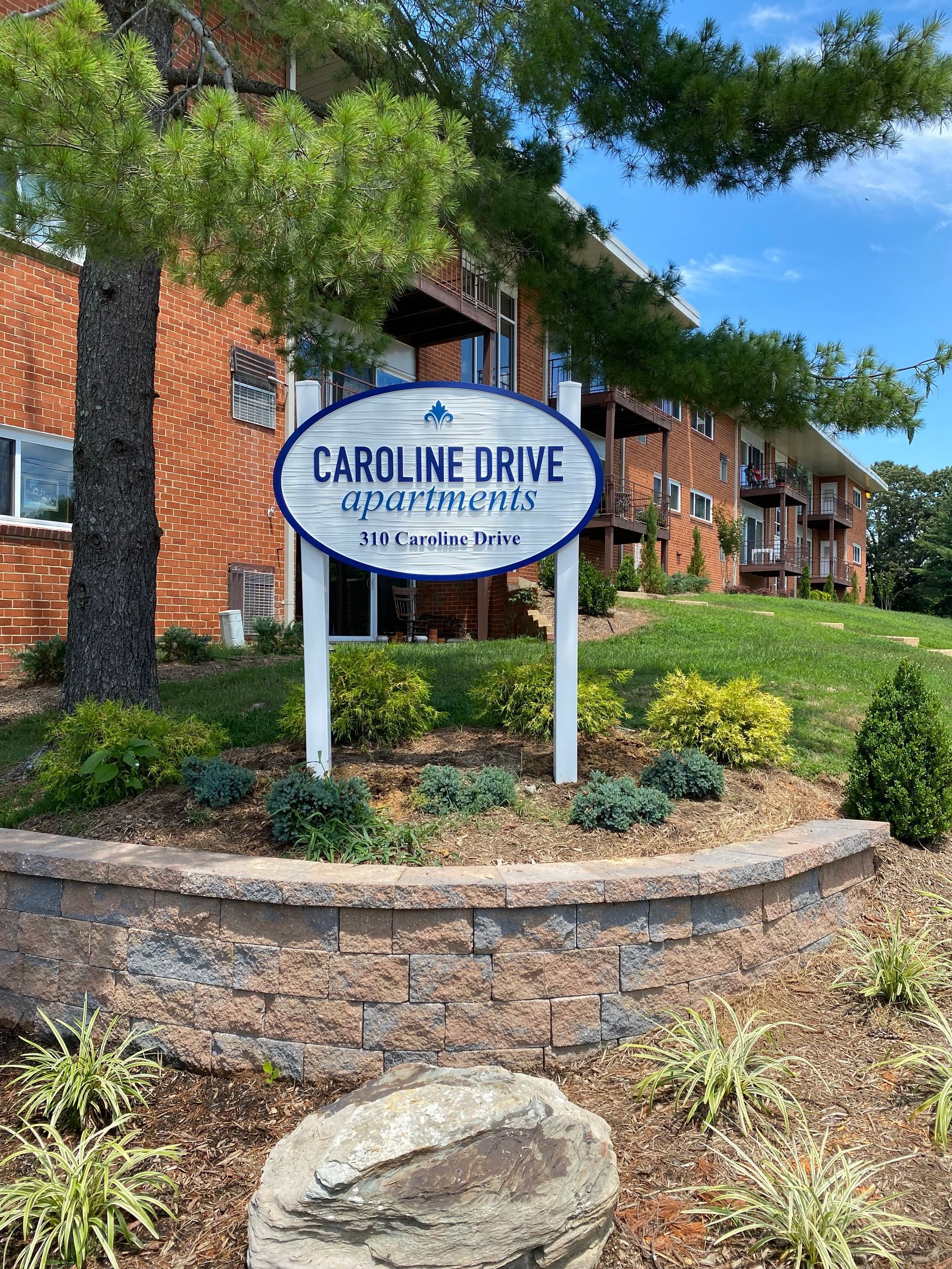 A sign for caroline drive apartments is in front of a brick building.