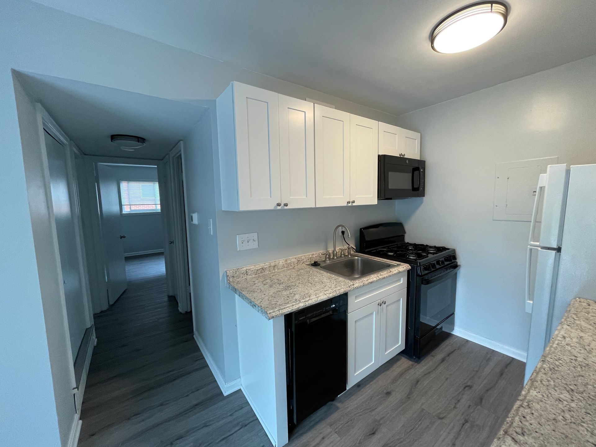A kitchen with white cabinets , black appliances , a sink and a refrigerator.