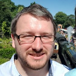 A profile photo of Andy from Beard Web Design - he has glasses and a short beard and is smiling in front of a train at Arley.