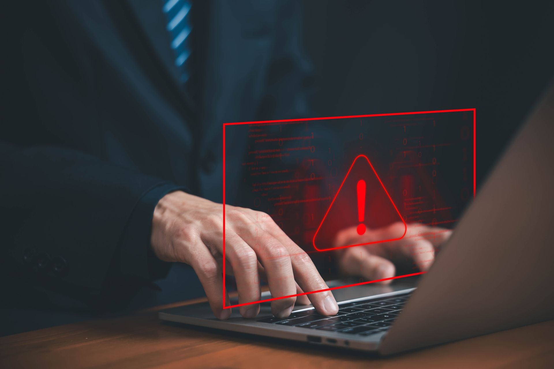 A man in a suit is sat at a desk using a laptop, a red warning sign is superimposed over the image.