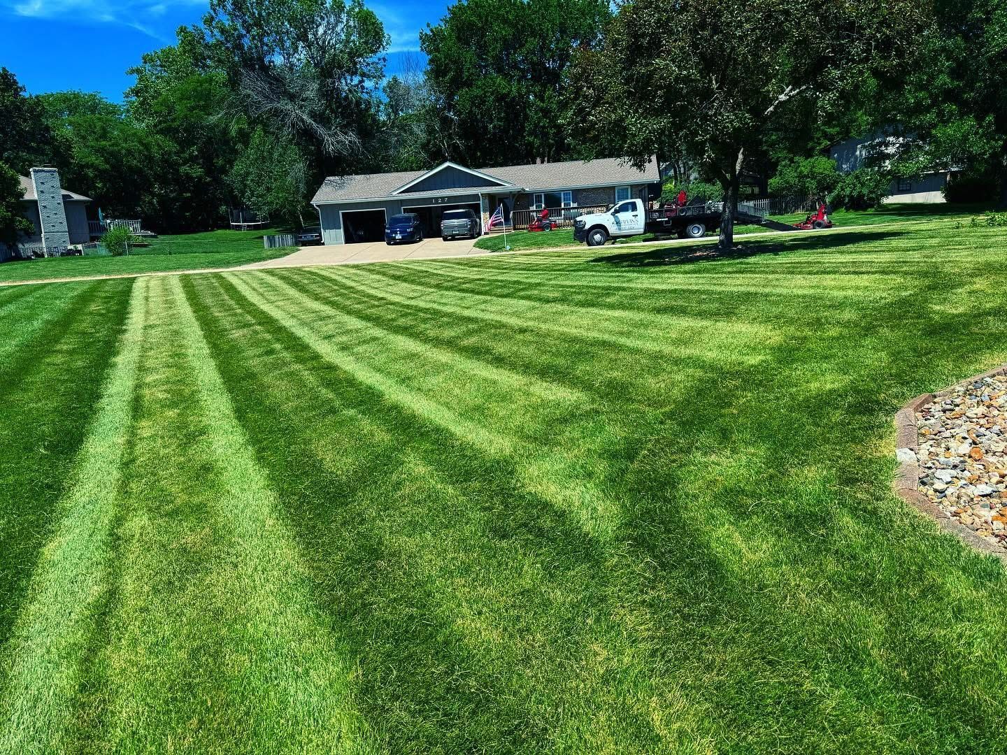 Lawn with distinct mowing patterns leading to a house with a blue car in the garage on a sunny day.