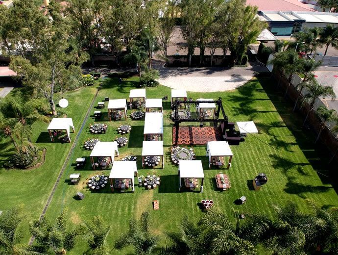 Vista aérea del jardín para eventos al aire libre con pabellones de techo blanco, mesas y un escenario central.