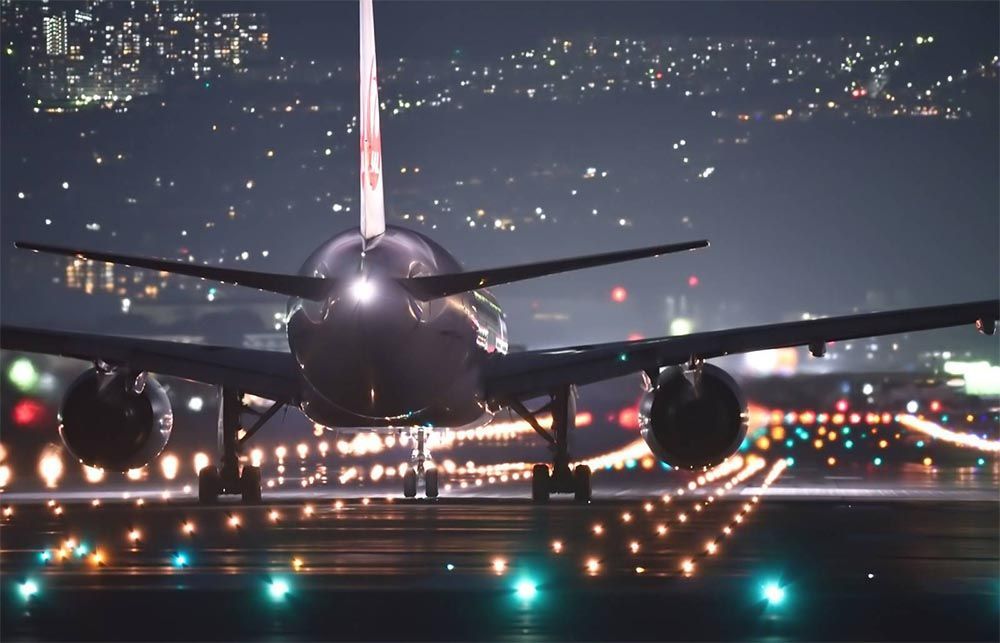 Avión aterrizando de noche en una pista iluminada, con luces de la ciudad de fondo.