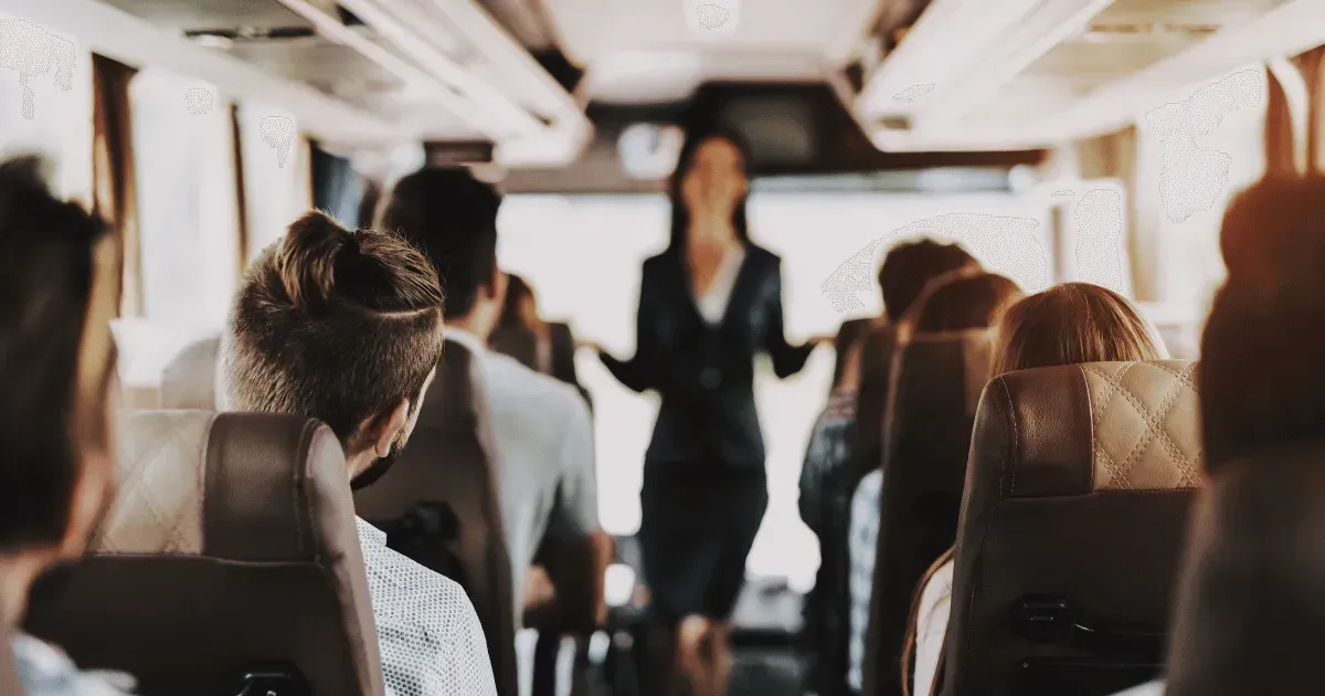 Una mujer con traje está parada en el pasillo de un autobús, de cara a los pasajeros.