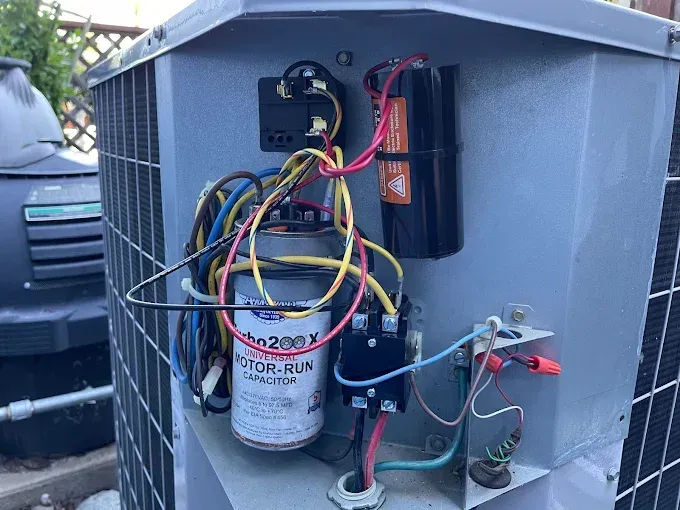 Open air conditioning unit with electrical components, wires, and capacitor.