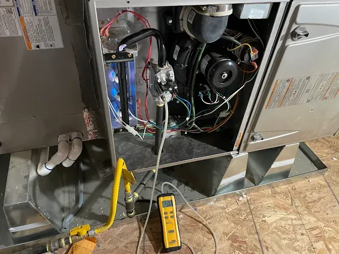 Furnace interior with a yellow gas line, testing equipment, and wiring.