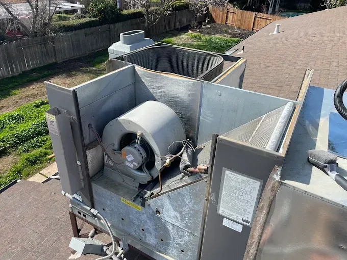HVAC unit on a roof with visible fan, ductwork, and maintenance tools.