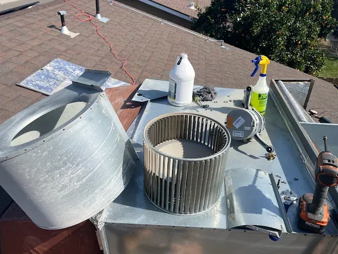 HVAC system components on a rooftop, including a blower wheel and housing, tools, and cleaning supplies.