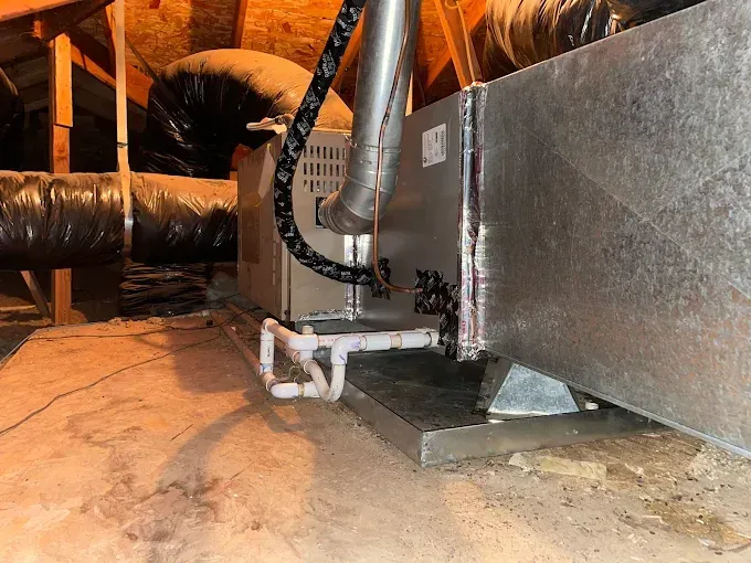 HVAC unit and ductwork in an attic, with water on the floor.