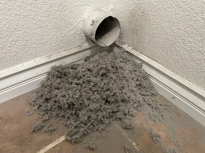 Lint pile on floor from dryer vent in corner of room.