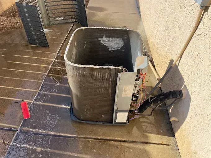 AC unit being cleaned outdoors, metal coil exposed, black fins removed.