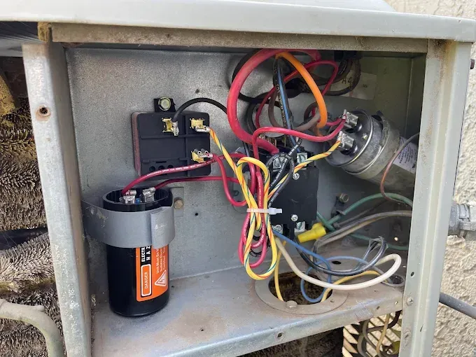 Open metal box containing HVAC electrical components with colored wires and capacitors.