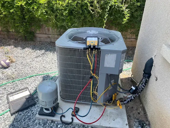 An outdoor air conditioning unit with connected wires and pipes, on a concrete slab in a gravel yard.