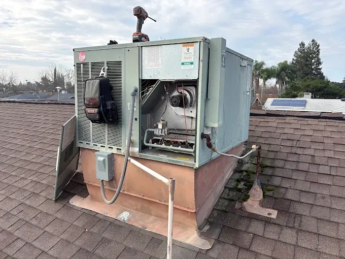 HVAC unit on a rooftop, open for repair. A power drill rests on top.