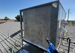 Cleaning an air conditioner on a rooftop with a pressure washer.