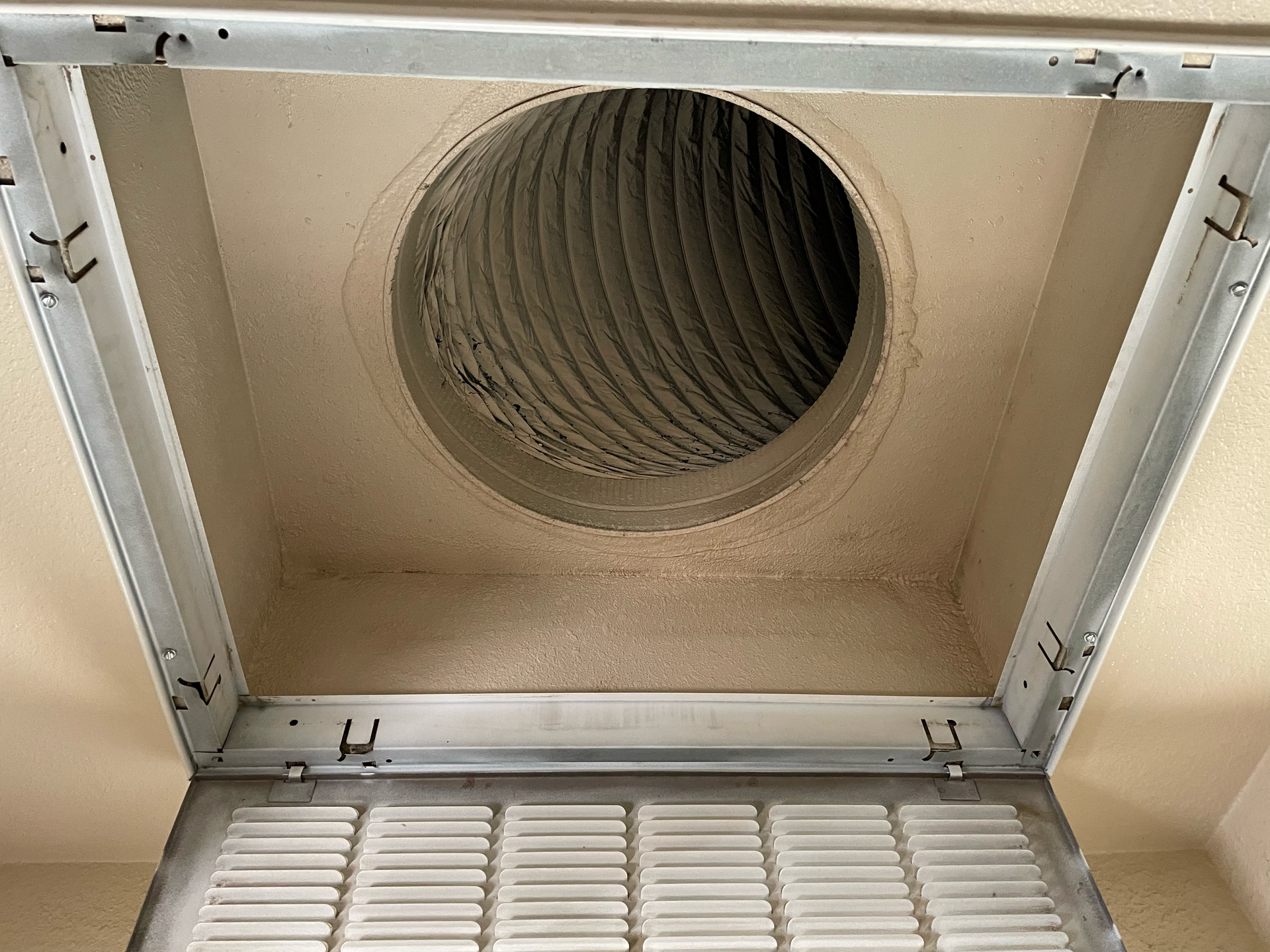 A metallic ventilation pipe bends away from a brick building against a blue sky.