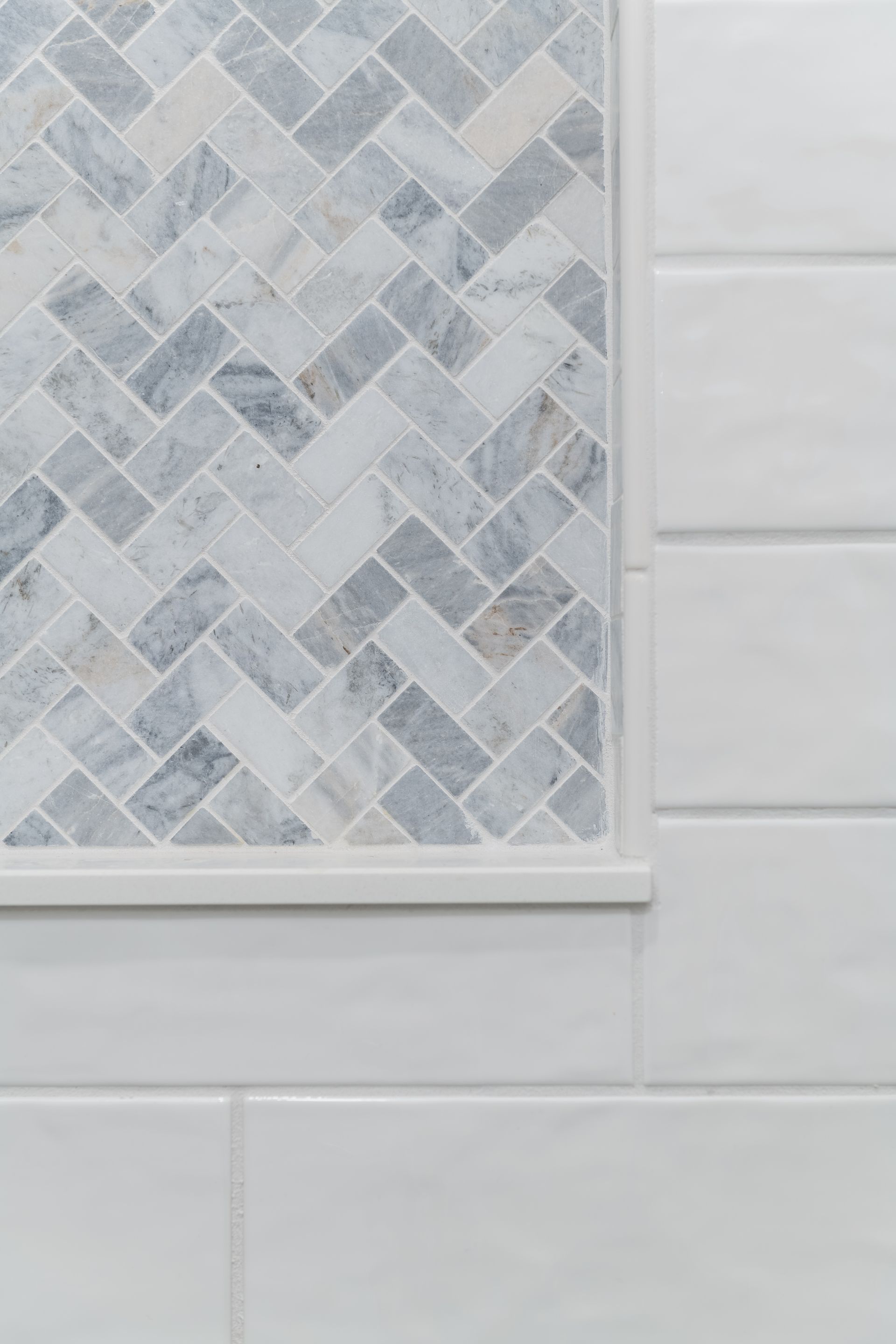 A close up of a white tile wall with a herringbone pattern.
