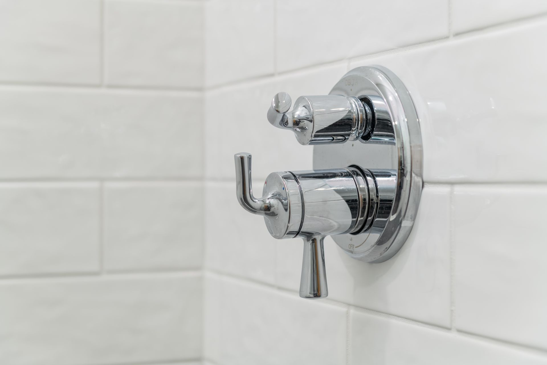 A close up of a shower faucet on a white tiled wall.