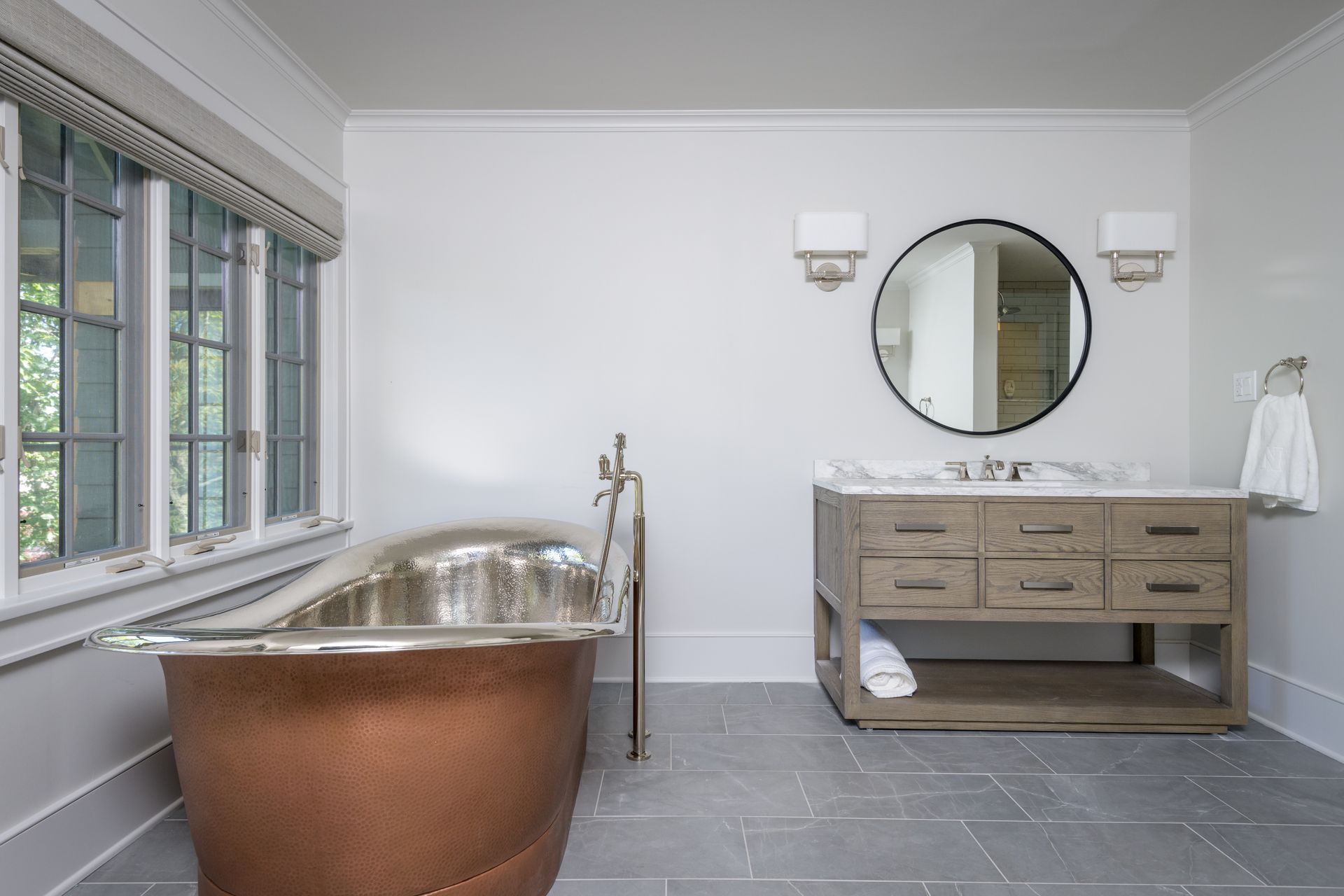 A bathroom with a copper tub , sink and mirror.