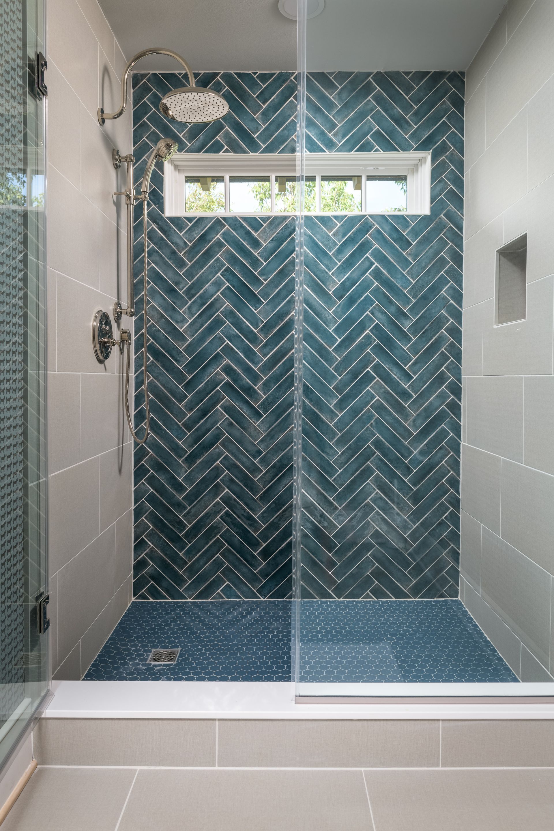 A walk in shower with blue tiles and a window.