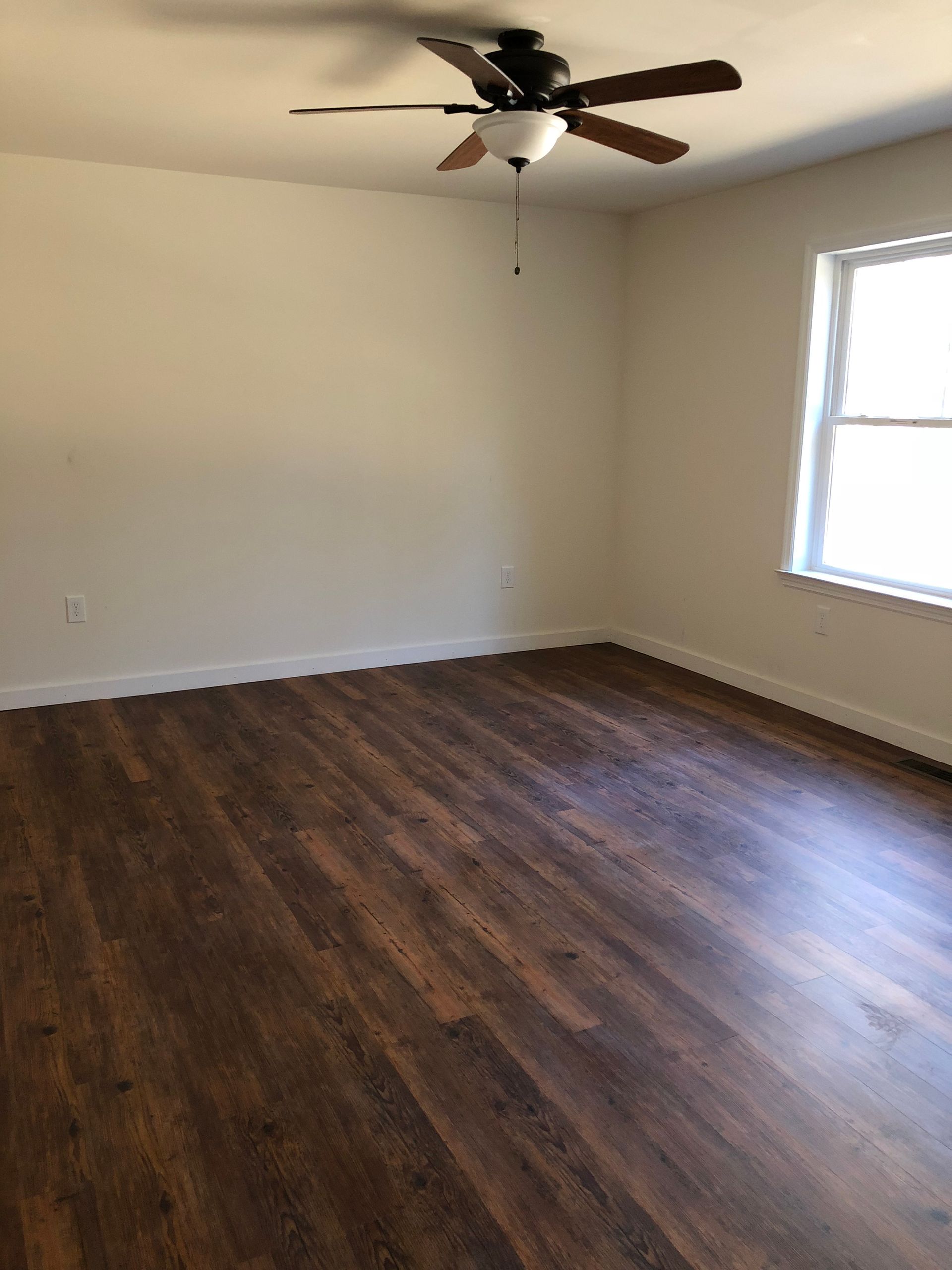 An empty room with a ceiling fan and a window.