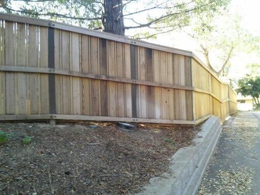 A wooden fence follows the downward slope of a hill above a stone curb and a paved path.