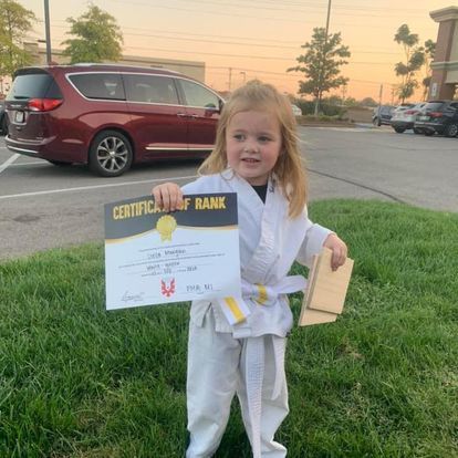 A little girl in a karate uniform is holding a certificate of rank