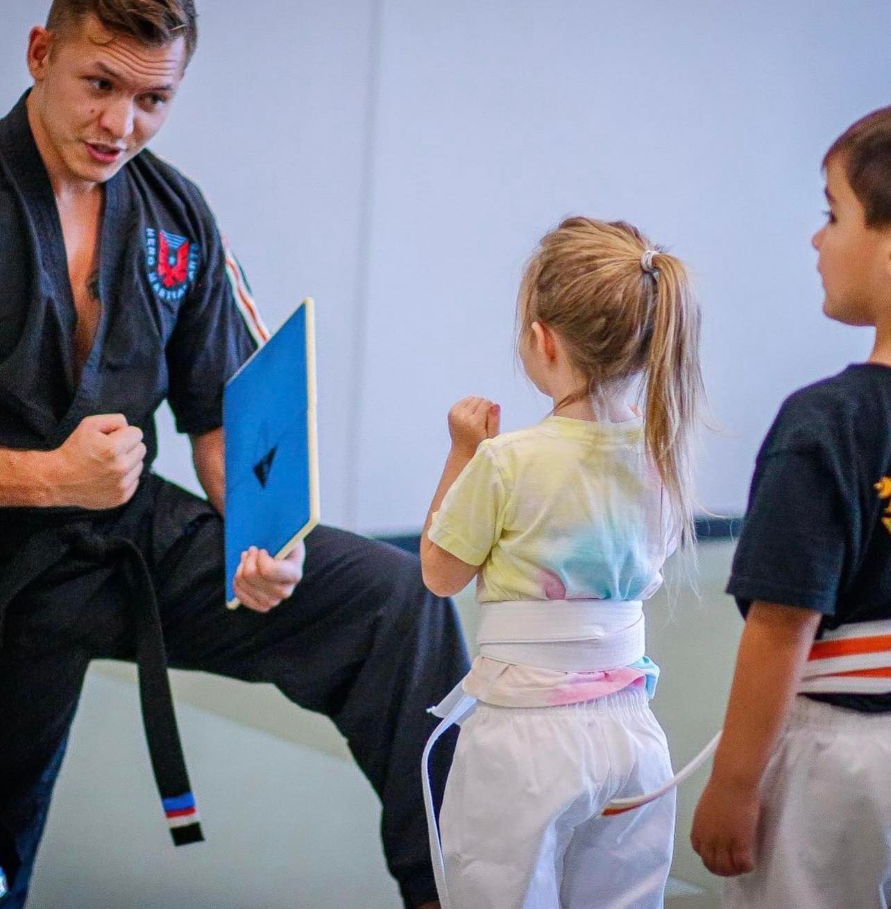 A man in a karate uniform is talking to two young children.