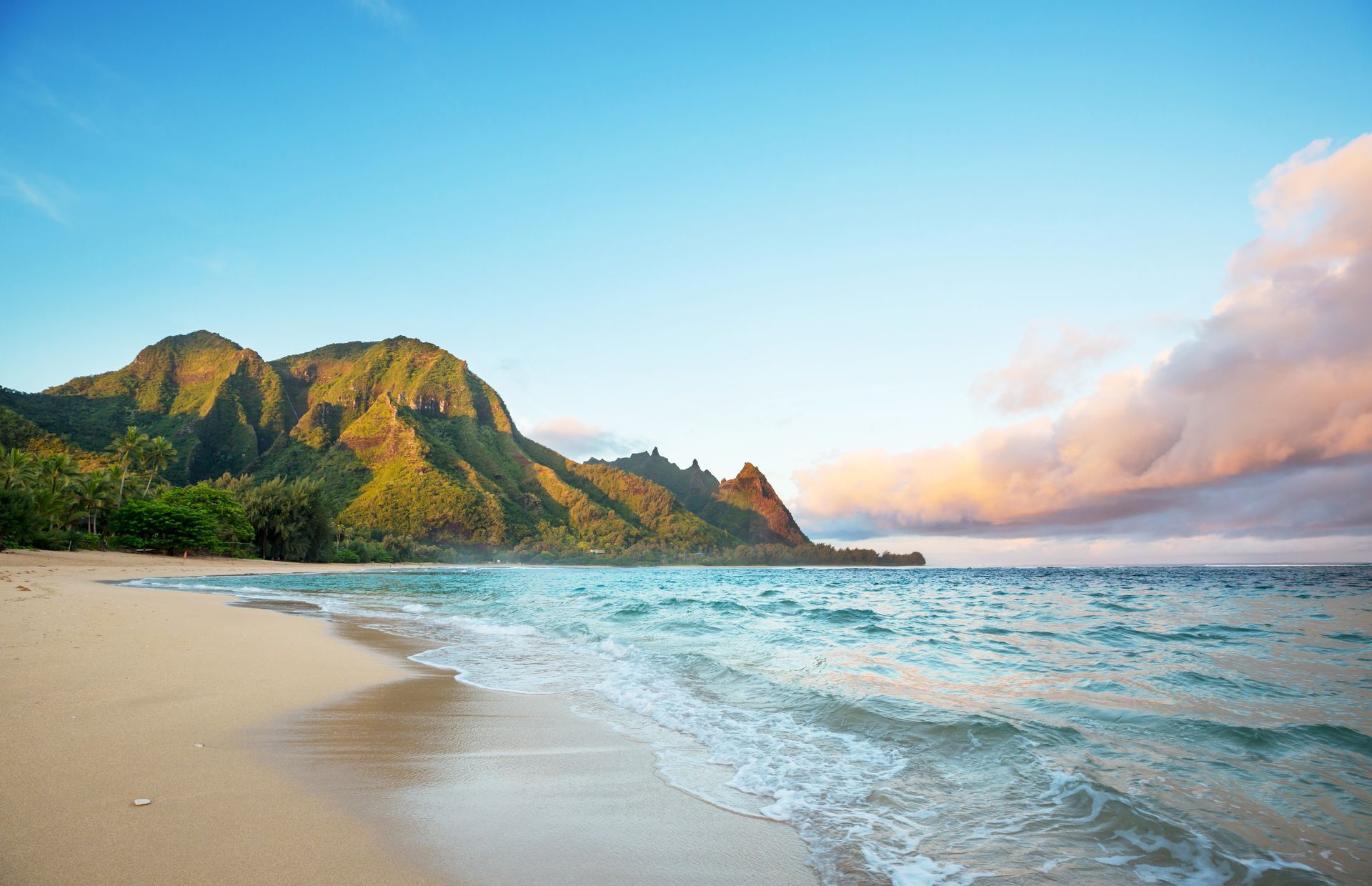 A beach with mountains in the background and waves crashing on the sand.