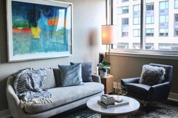A living room with a couch , chair , coffee table and painting on the wall.
