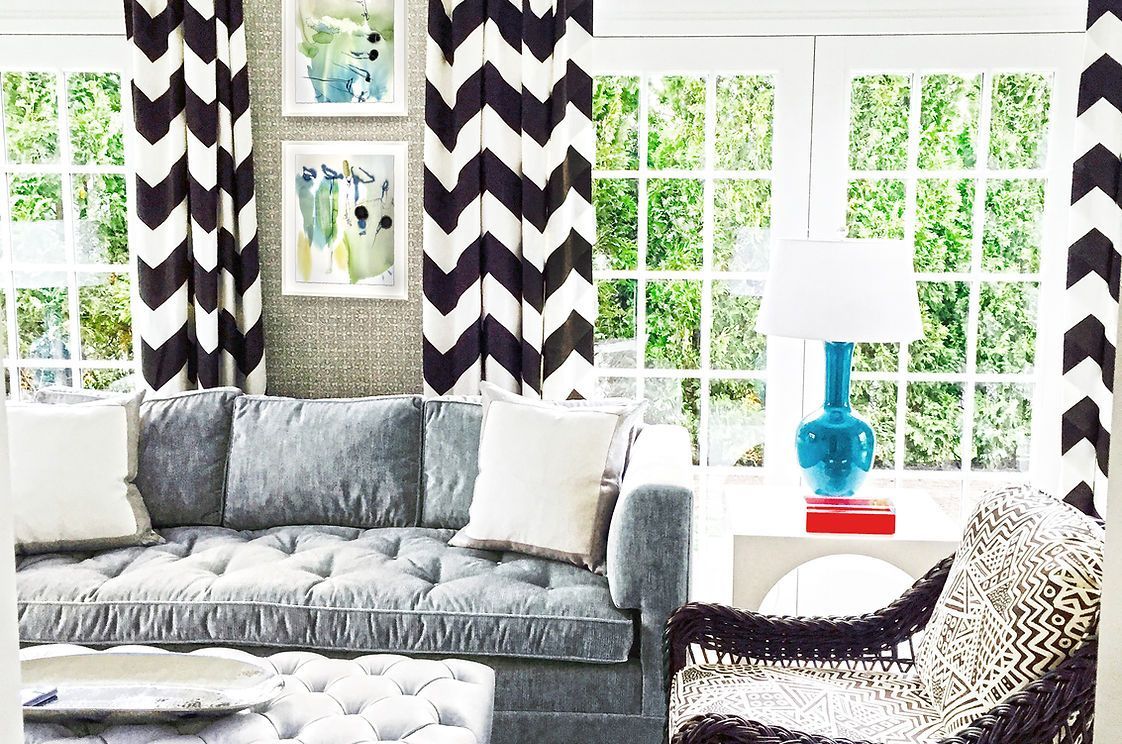 A living room with a couch , chair , ottoman and chevron curtains.