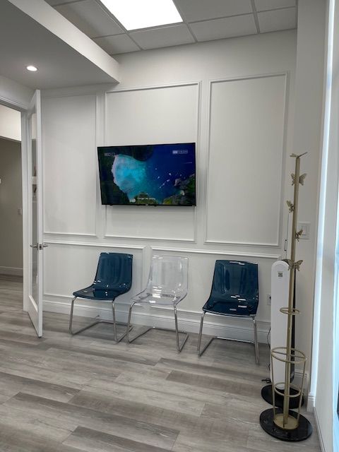 Modern waiting room with blue chairs, wall-mounted TV, and coat rack on a light wood floor
