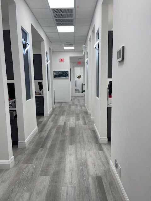 Empty office hallway with gray flooring, white walls, and ceiling lights, leading to a doorway.