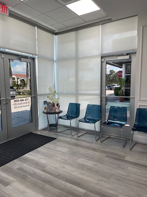 Bright waiting room with blue chairs, gray wood flooring, and glass doors/windows at an office entrance