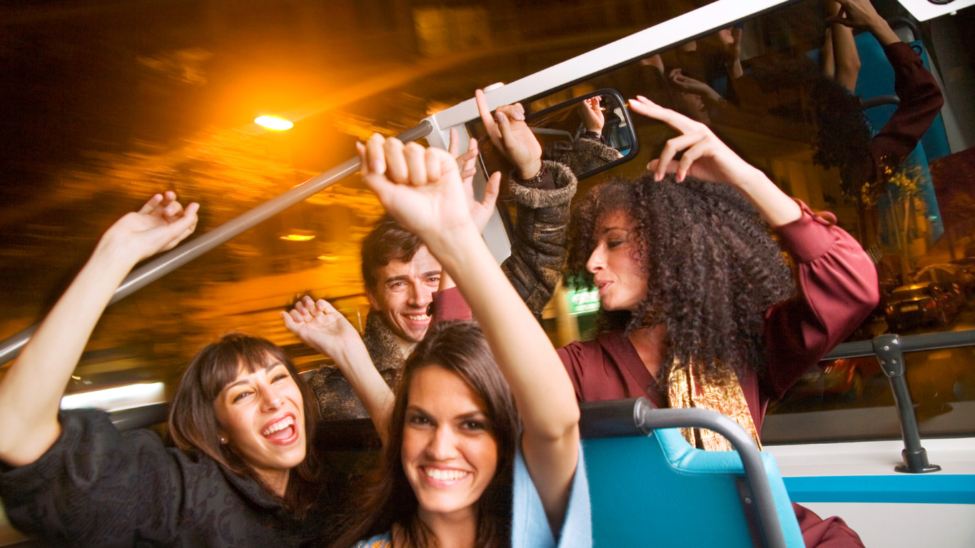 A group of people are sitting on a bus with their arms in the air.