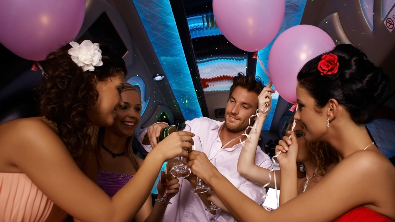A group of people are toasting in a limousine with pink balloons.