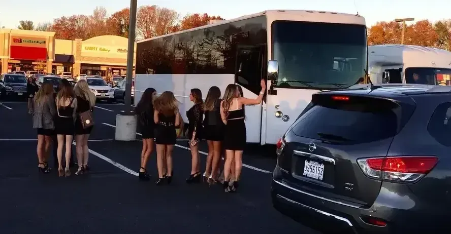 A group of women are standing in front of a bus in a parking lot.