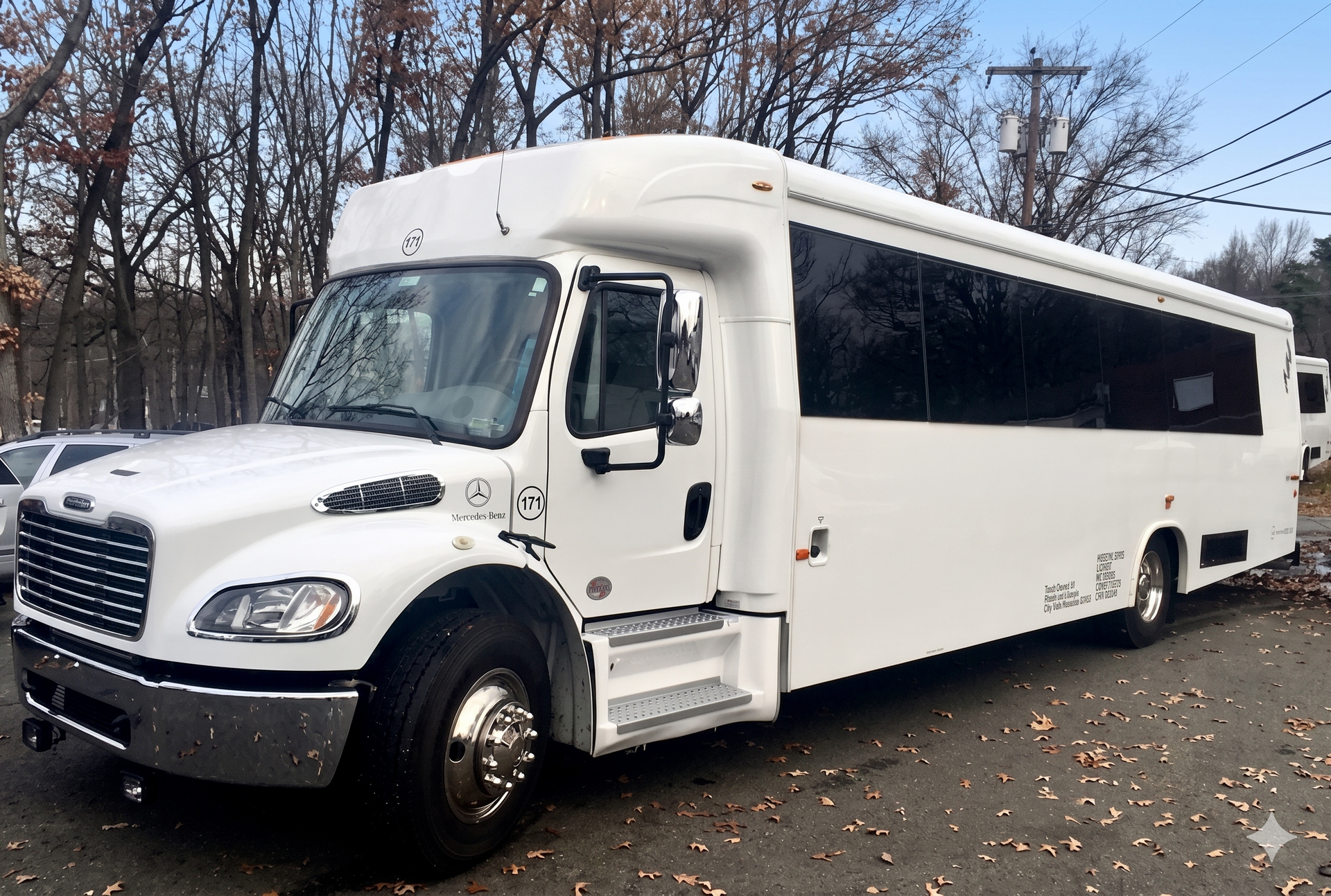 A white, full-size shuttle bus parked on an asphalt lot with trees in the background.
